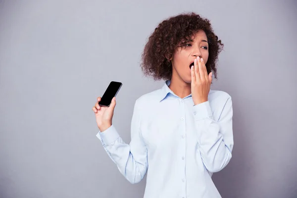 Mujer afroamericana bostezando mientras sostiene el teléfono inteligente — Foto de Stock