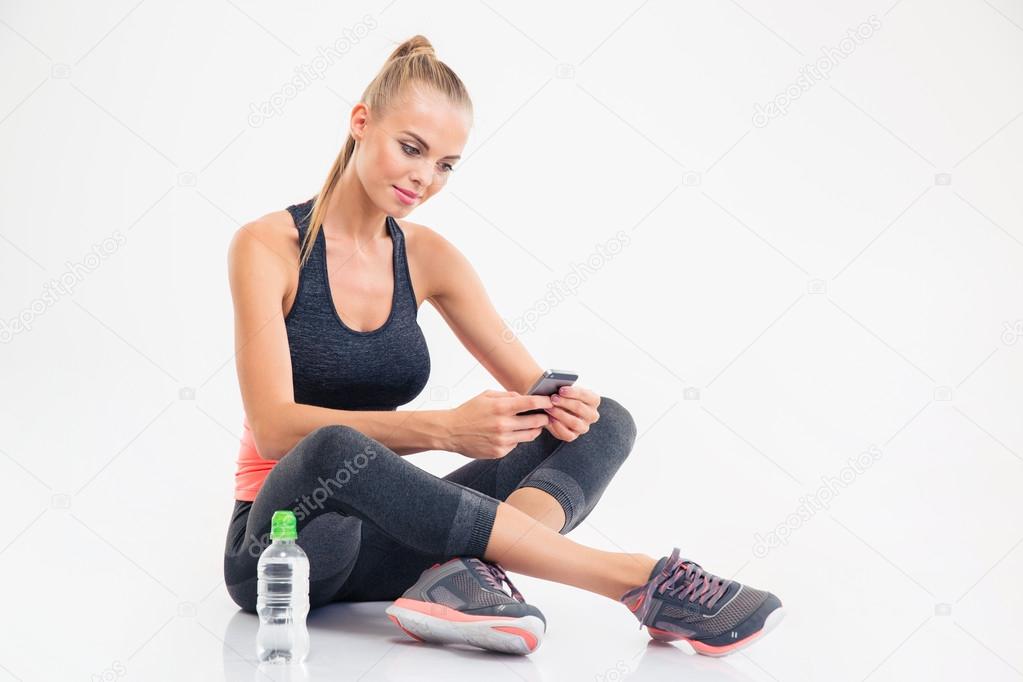 Fitness woman sitting on the floor and using smarpthone