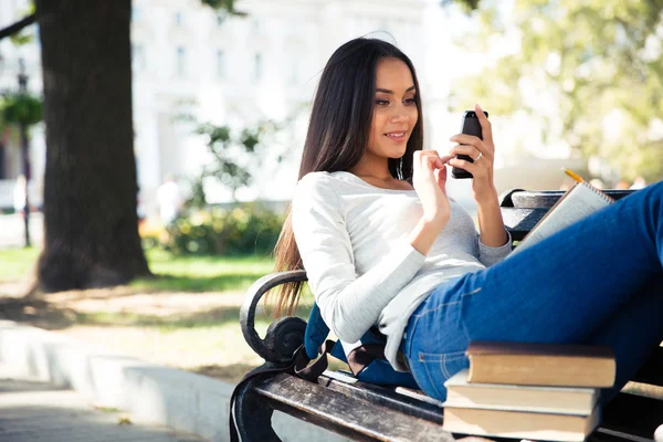 Kvinnlig student liggande på bänken och använder smartphone — Stockfoto