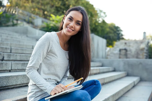 Flicka sitter i staden trappan med penna och anteckningsblock utomhus — Stockfoto