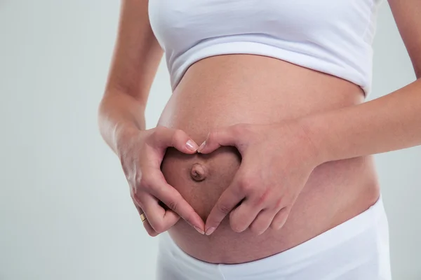 Pregnant woman making heart gesture on the belly — Stock Photo, Image