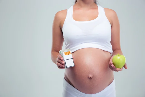 Pregnant woman choosing beetwin cigarettes and apple — Stockfoto