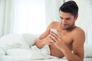 Adam yatakta akıllı telefon kullanıyor.
