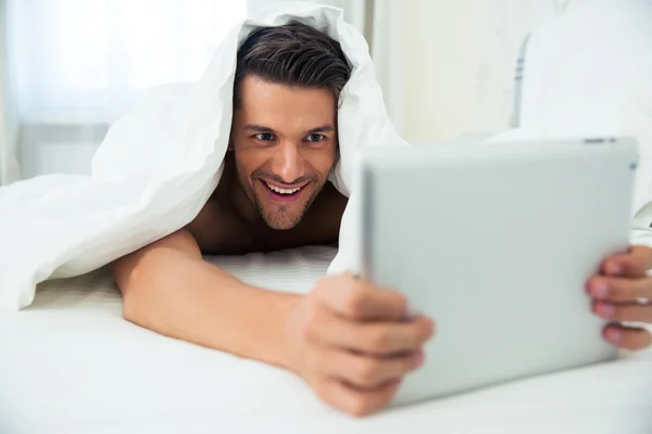 Homme couché sous couverture et utilisant une tablette — Photo