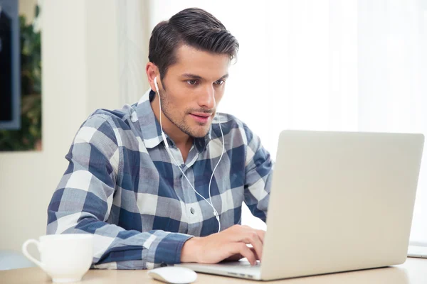 Homme utilisant un ordinateur portable avec écouteurs à la maison — Photo