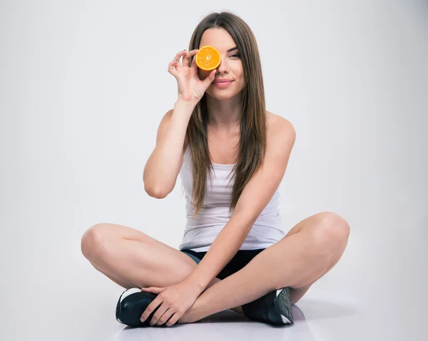 Chica sentada en el suelo y cubriendo un ojo con naranja — Foto de Stock
