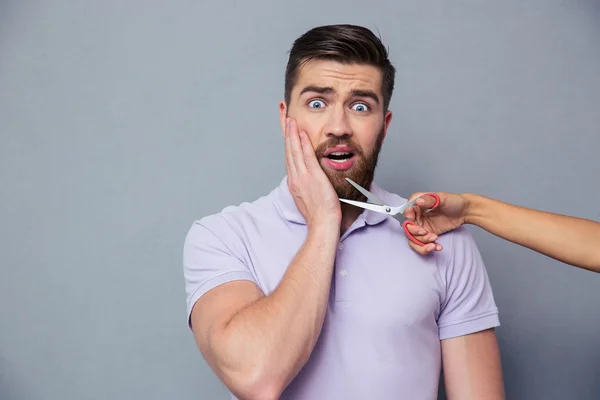 Hombre mirando asustado mientras manos femeninas sosteniendo tijeras cerca de la barba — Foto de Stock