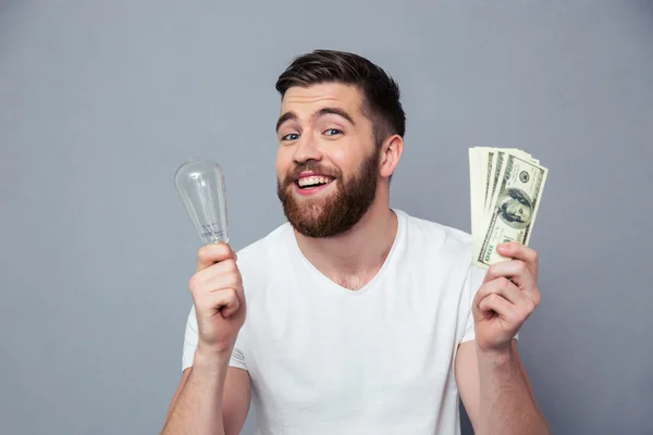 Улыбающийся мужчина держит лампочку и долларовые купюры — стоковое фото