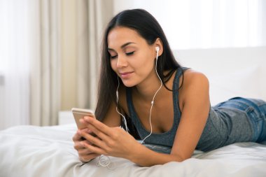 Evde kulaklık ile akıllı telefon kullanan kız