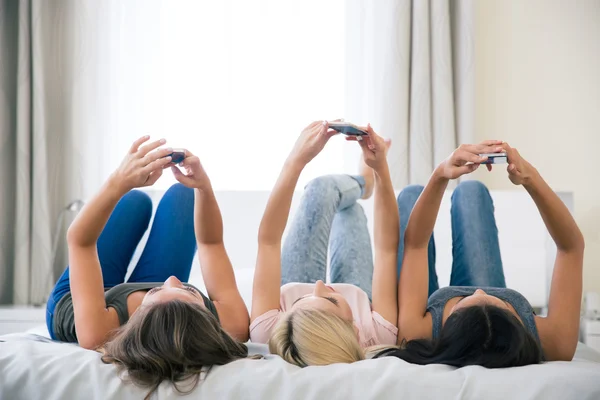 Chicas acostadas en la cama y usando teléfonos inteligentes —  Fotos de Stock