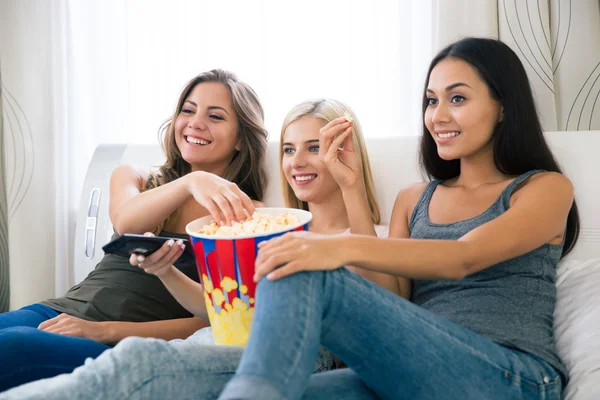 Três namoradas felizes comendo pipocas e assistindo tv — Fotografia de Stock