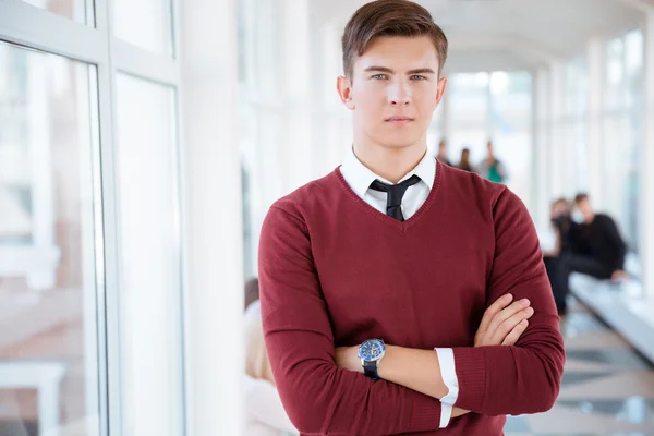 Male student standing with arms folded in university hall — Stock Photo, Image