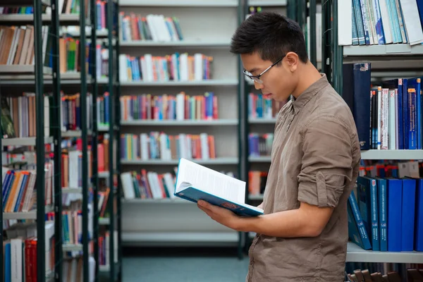 Männlicher Student liest Buch in Bibliothek — Stockfoto