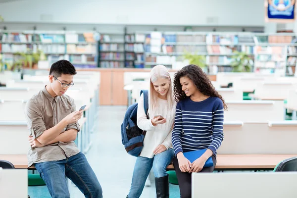 Šťastní studenti pomocí smartphone v knihovně — Stock fotografie