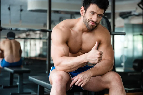 Muskulöser Mann sitzt auf der Bank und zeigt Daumen hoch — Stockfoto