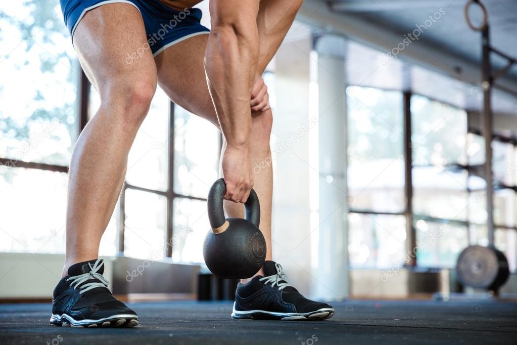 Sporty man hands and legs lifting kettle ball