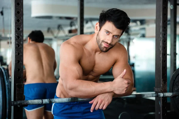 Hombre musculoso mostrando el pulgar hacia arriba en gimnasio de fitness —  Fotos de Stock