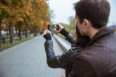 Couple making photo on smartphone of autumn park clipart