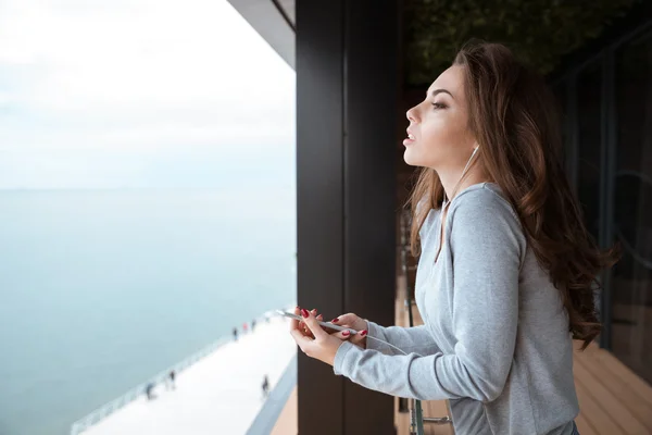 Νεαρή γυναίκα στέκεται στο μπαλκόνι και να ακούτε μουσική — Φωτογραφία Αρχείου