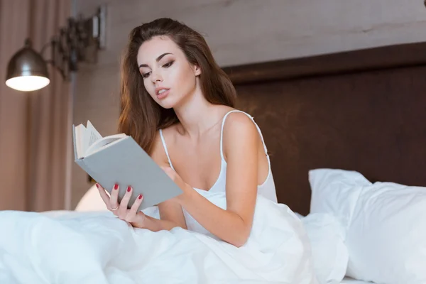 Güzel genç kadın yatağın üstüne oturan okuma — Stok fotoğraf