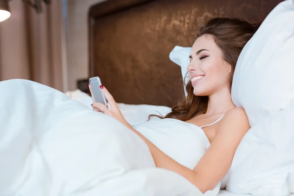 Девушка с сотовым телефоном лежит в постели — стоковое фото