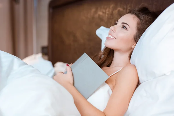 Jovem mulher sonhando em sua cama segurando o livro — Fotografia de Stock