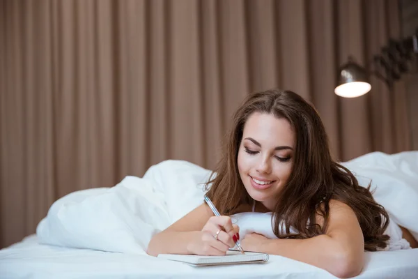 Vrouw maken van aantekeningen in Kladblok liggend op het bed — Stockfoto