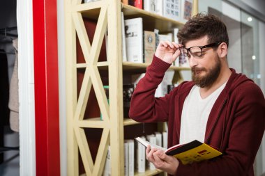 Genç adam kitap ayakta bookshelf yakınındaki okuma sakallı