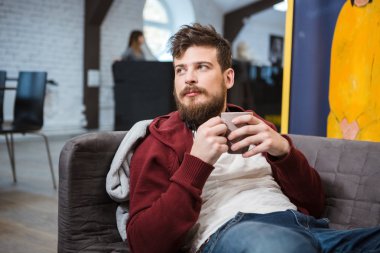 Bardak çay ile kanepede yatan yakışıklı genç adam