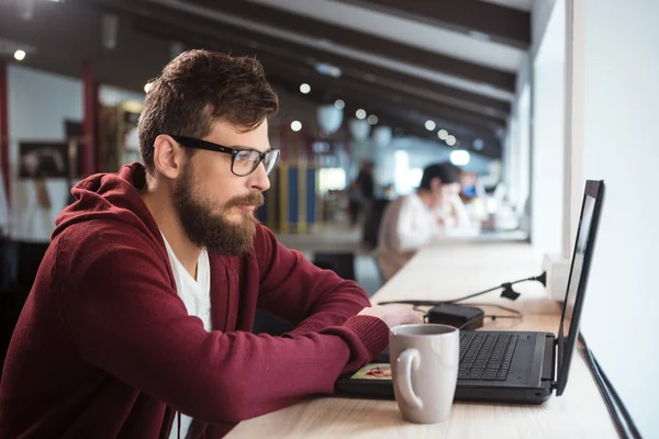 Hombre joven en gafas sentado y usando el ordenador portátil — Foto de Stock