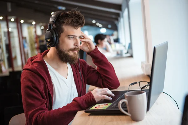 Menino com barba usando laptop e ouvindo música — Fotografia de Stock