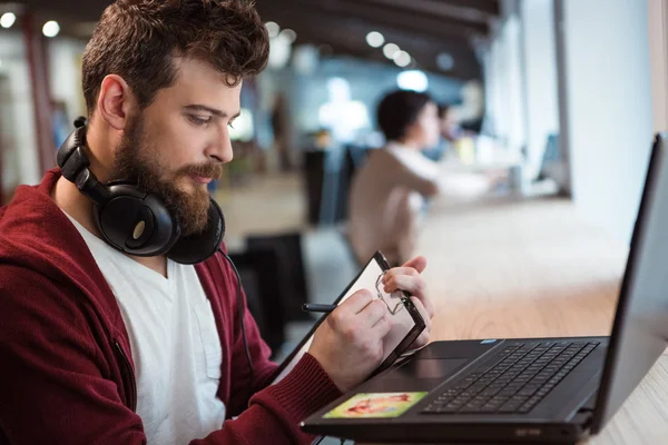 Bebaarde man schrijven op Klembord en met behulp van laptop — Stockfoto