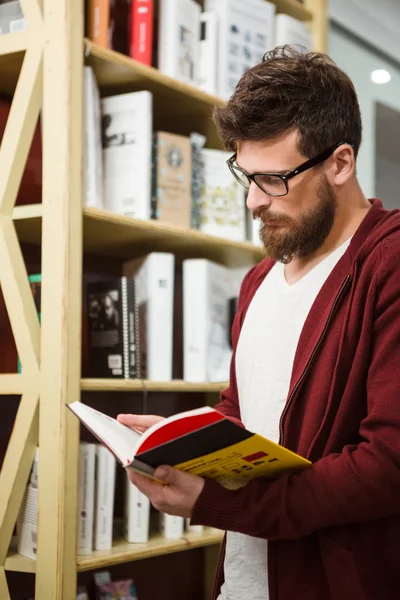 Przystojny student w okularach czytanie książki w bibliotece — Zdjęcie stockowe