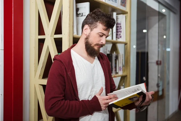 Skoncentrowany facet trzyma okulary i czytanie książki w bibliotece — Zdjęcie stockowe