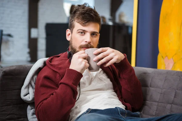 Relajado chico sentado en el sofá y beber café —  Fotos de Stock