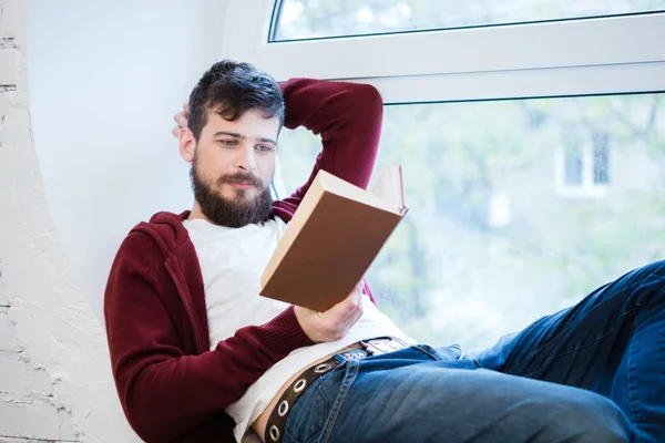 Ontspannen jonge kerel liggend op de vensterbank en lezen — Stockfoto