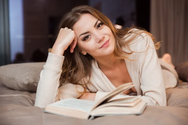 Chica sonriente acostada en la cama y leyendo —  Fotos de Stock