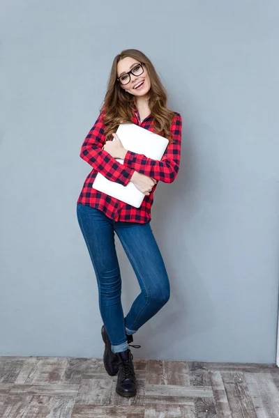 Vrolijk meisje in glazen poseren en glimlachend knuffelen laptop — Stockfoto