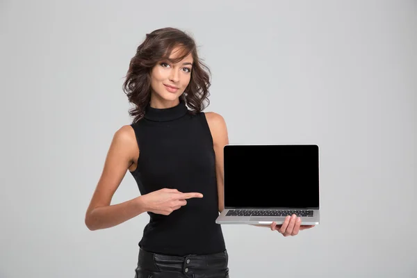 Mujer joven sonriente apuntando en la pantalla del ordenador portátil en blanco — Foto de Stock