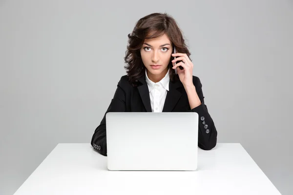 Confident business woman working using laptop and talking on cellphone — Stock Photo, Image