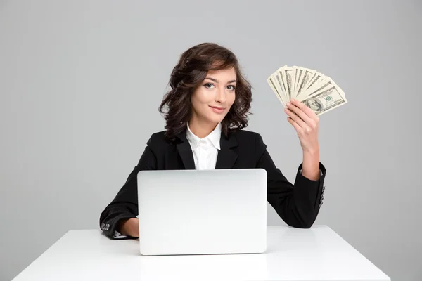Красивая молодая женщина использует ноутбук и показывает деньги — стоковое фото