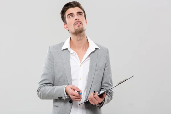 Young man thinking holding clipboard — Stock Photo, Image
