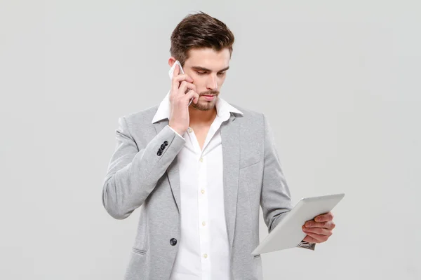 Молодой бизнесмен разговаривает по мобильному телефону и пользуется планшетом — стоковое фото