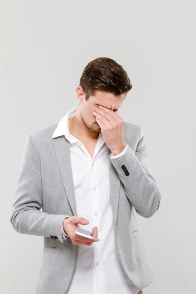 Joven deprimido sosteniendo el celular y frotando los ojos — Foto de Stock