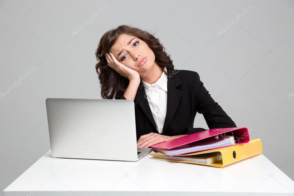 Bored sad young woman using laptop and working with documents