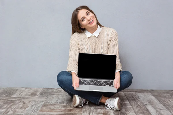 Cheerful girl sitting on floor and holding blank laptop screen — Stock Photo, Image