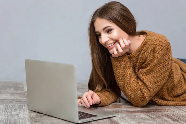 Mujer joven bastante alegre acostado en el suelo usando el ordenador portátil — Foto de Stock