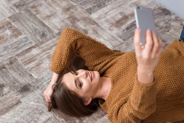 Mooi meisje op houten vloer liggen en het maken van selfie — Stockfoto