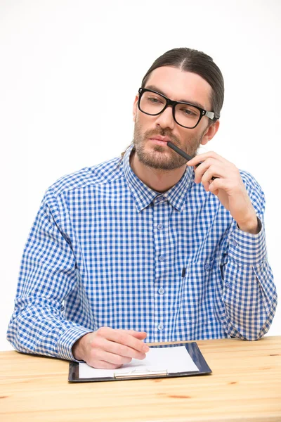 Myšlení mladý muž v brýlích, sedící u stolu — Stock fotografie
