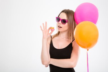 Amusing young woman in pink sunglasses eating macaroons
